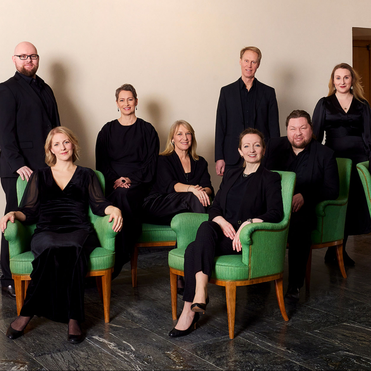 En grupp svartklädda kvinnor och män sitter samlade i en grön soffgrupp.