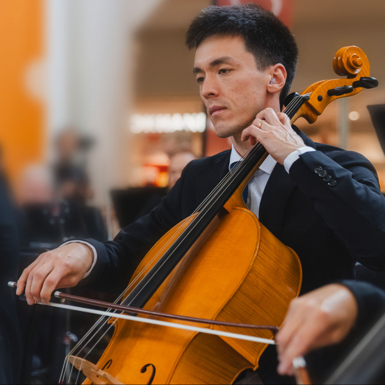 En cellist sitter och spelar med blicken fäst i noterna.