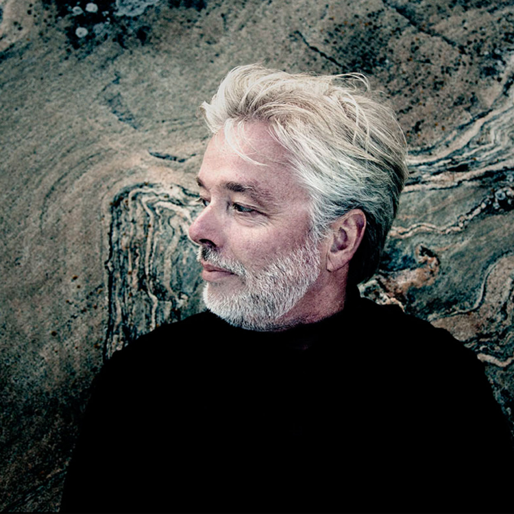 Jukka-Pekka Saraste syns i profil. Han har grått välansat skägg och är fotad mot en bergvägg.