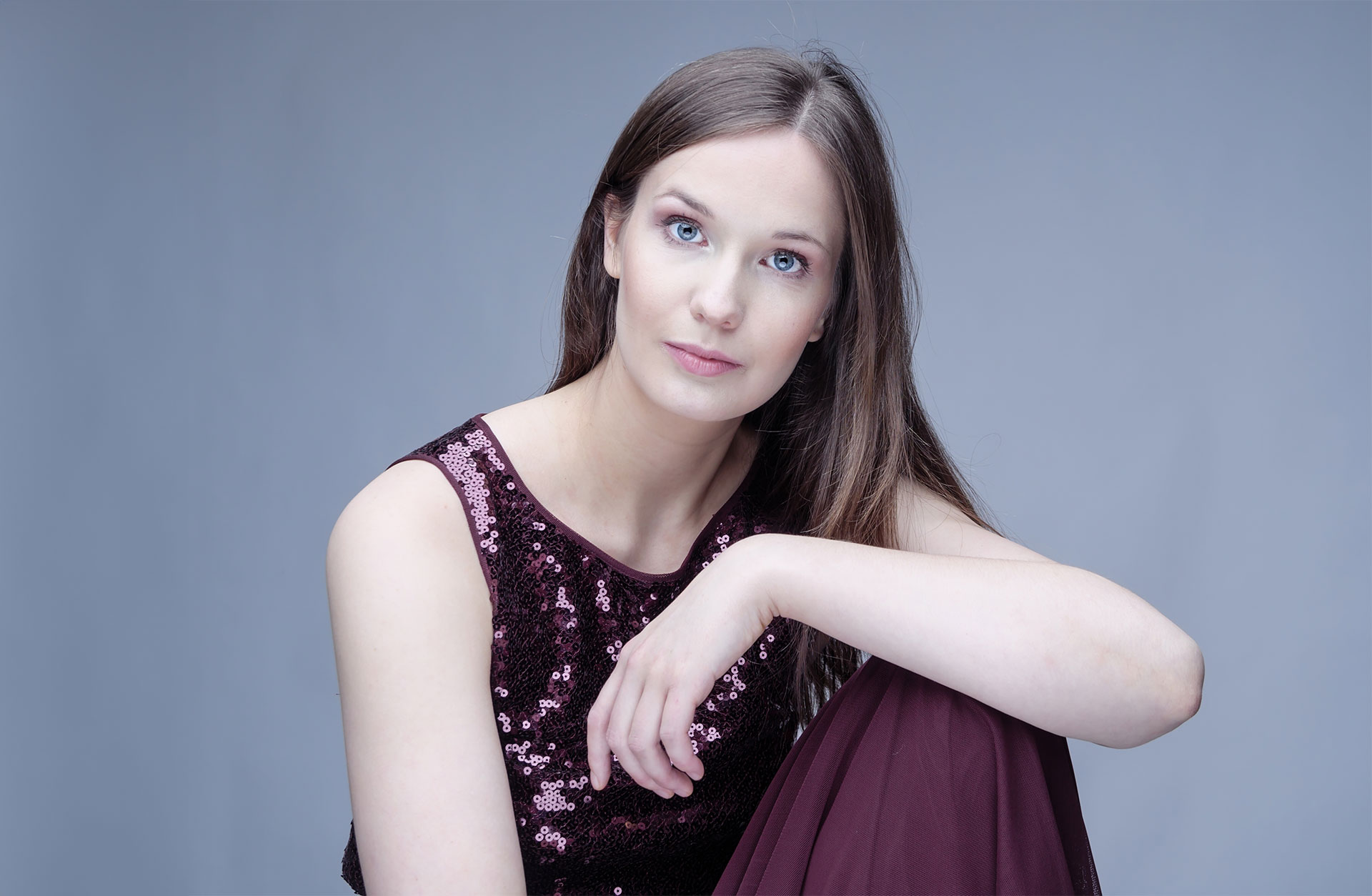 Porträtt av en ung med långt hår som sitter med armen stödd på ett uppdraget knä. Hon tittar in i kameran.