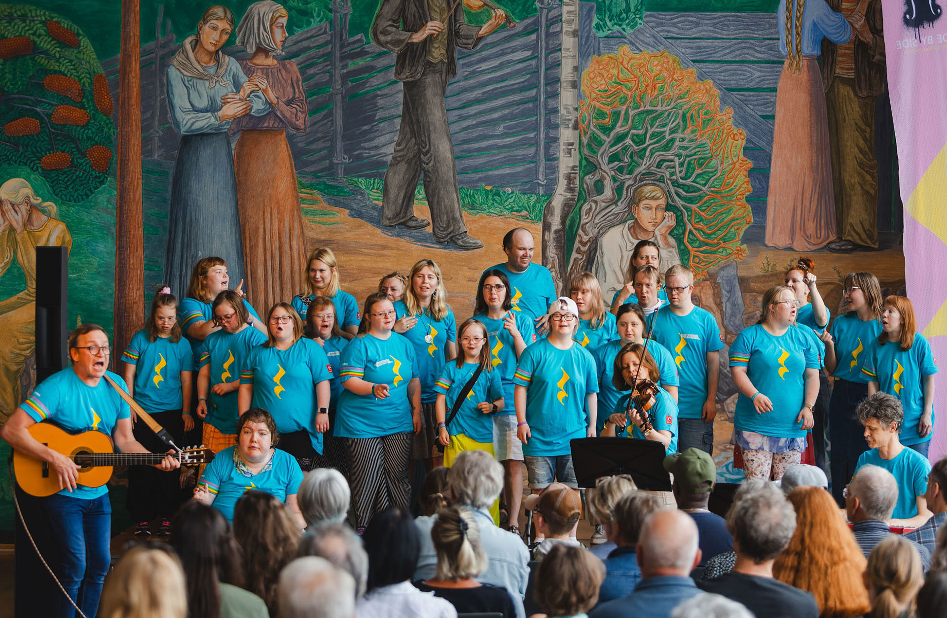 Körsångare tillsammans med en gitarrist och en violinist.