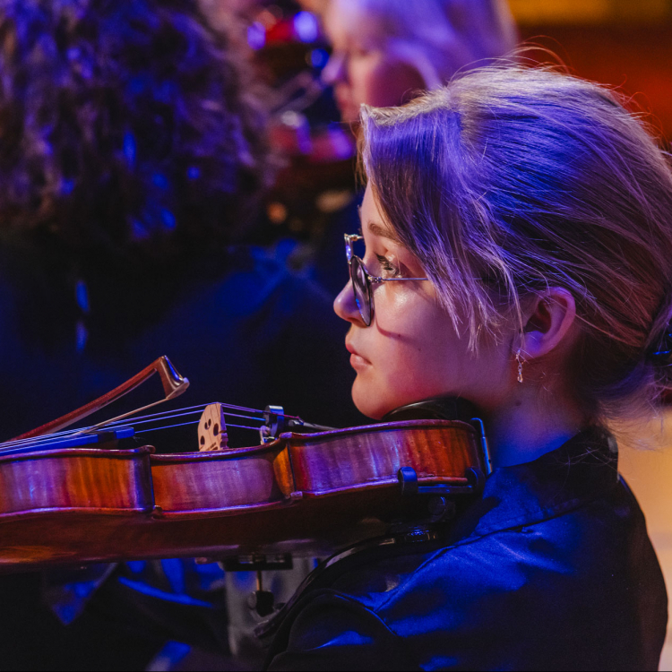 Ung tjej sitter i profil i orkestern och spelar violin.