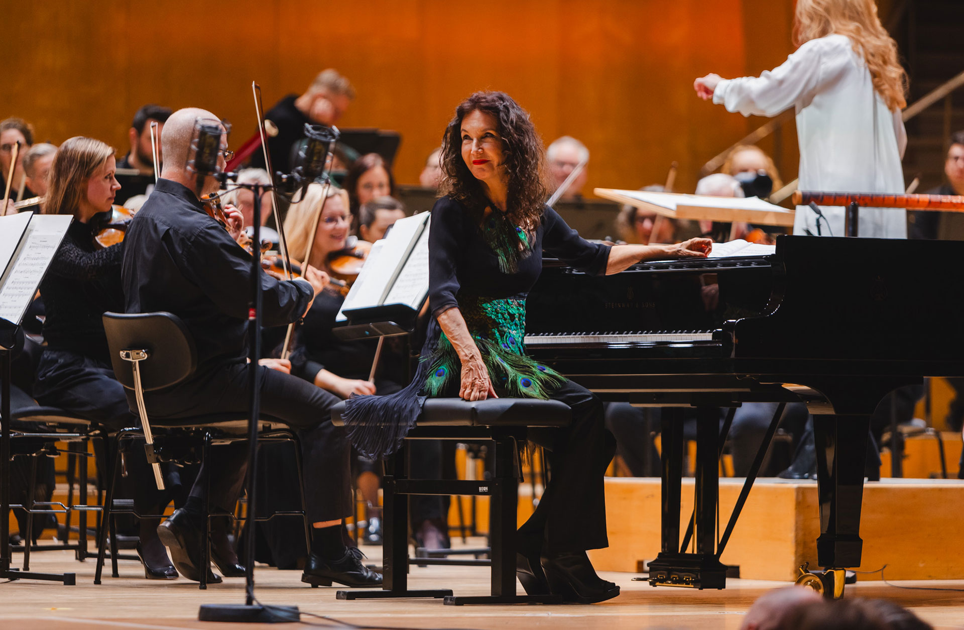 Kvinna med långt mörkt hår vänder sig om vid flygeln och ler.