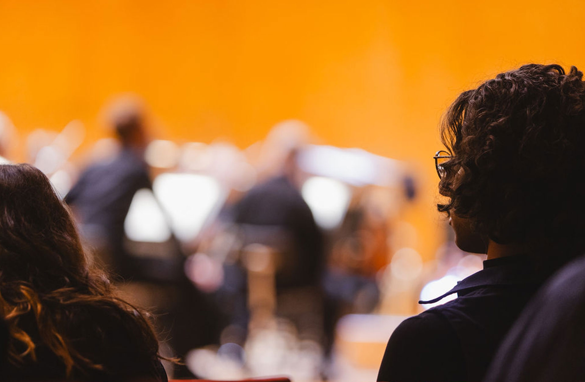 Siluett av två personer som sitter i konsertsalen och lyssnar.