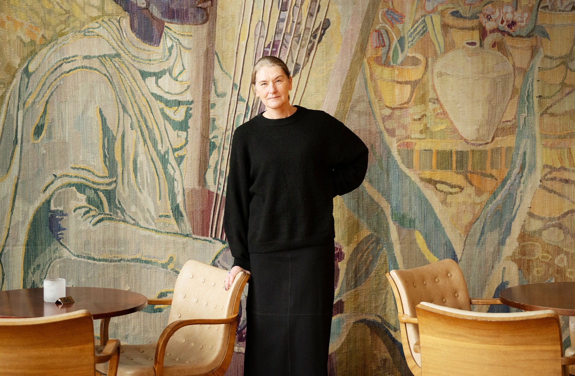 En glad Anna-Karin Larsson står vid gobelängen i Götaplatsfoajen. Hon tittar allvarligt in i kameran.