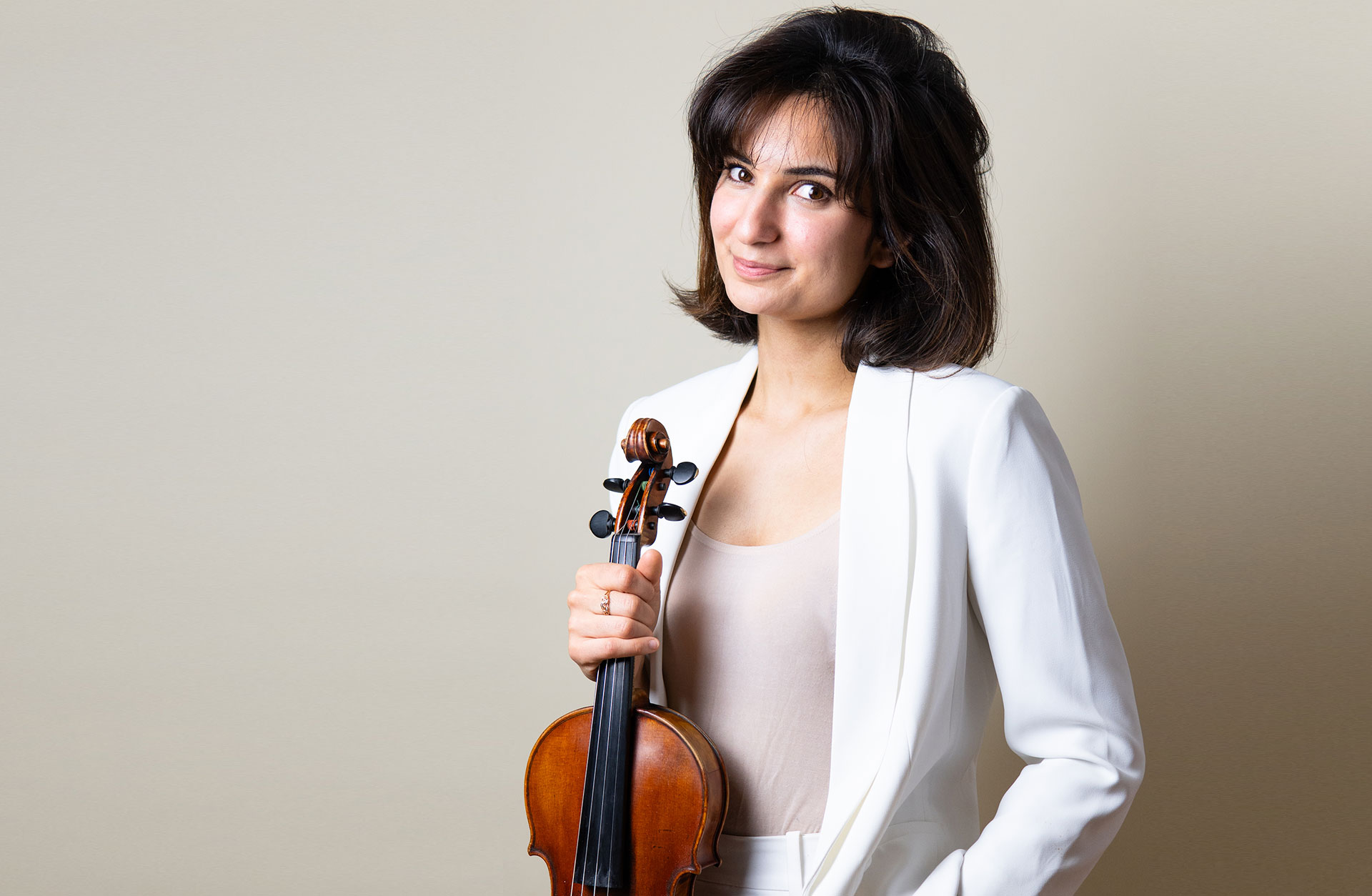 Violinisten Ava Bahar ler i vit kostym med instrumentet i sin hand.