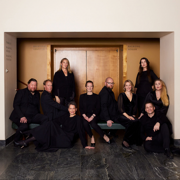 Medlemmarna i Vokalensemblen sitter på en bänk framför dörren till Stenhammarsalen. De är klädda i svart och tittar på kameran.
