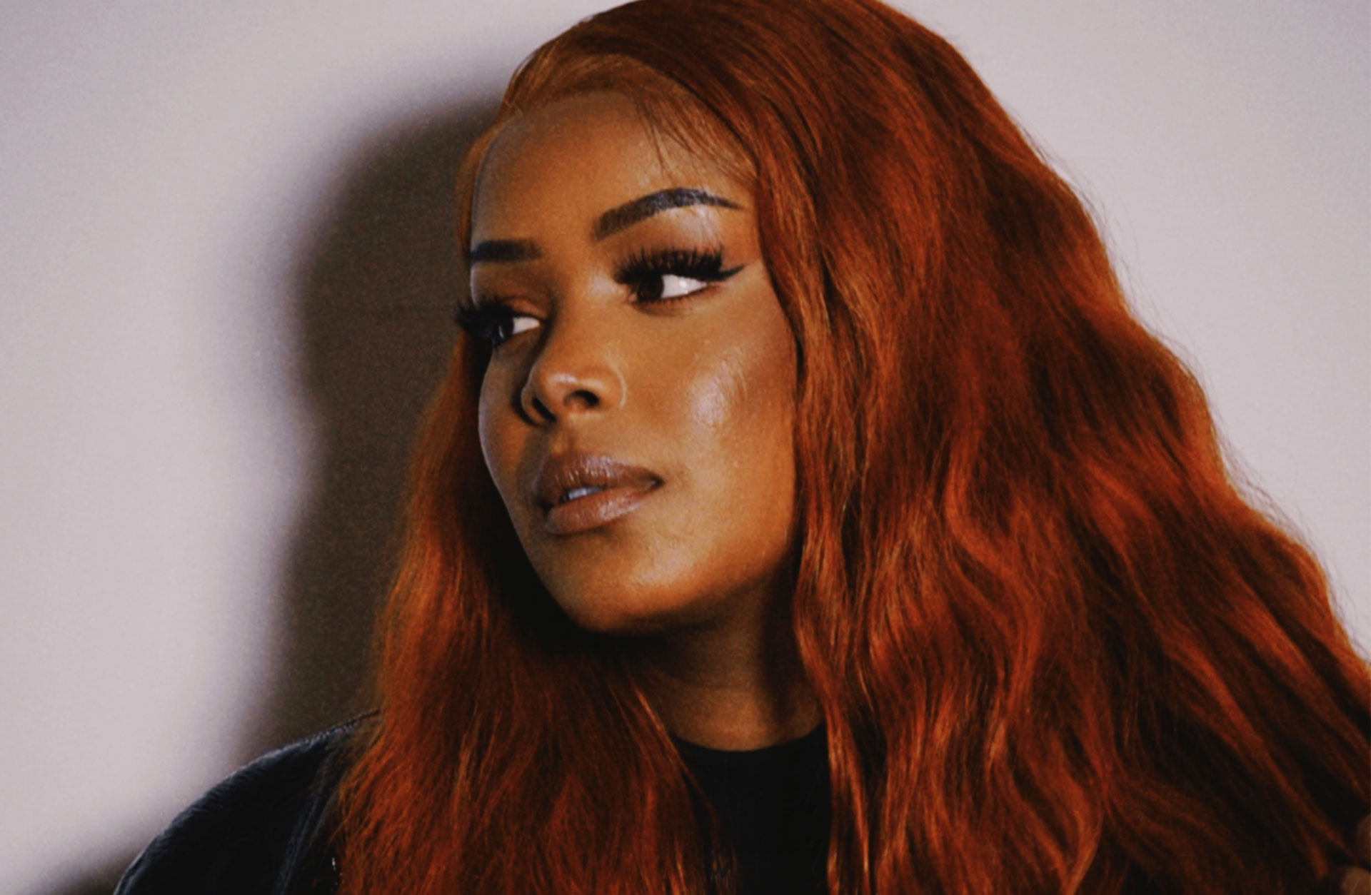 Imenella tittar åt sidan. Hon har rött långt hår och mörka ögon.