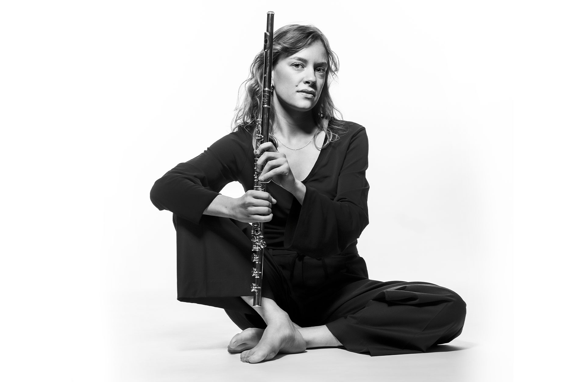 Svartvit bild där Laura Michelin sitter på golvet med sin flöjt i famnen.