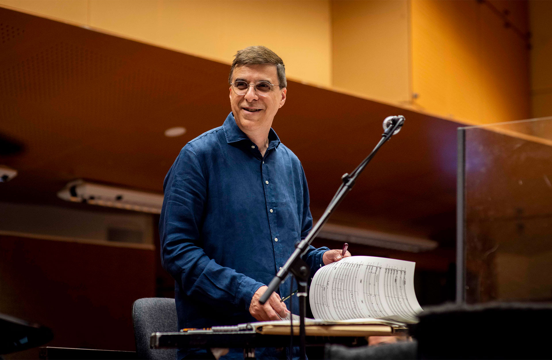 En ledigt klädd Vince Mendoza på pulten med ett partitur framför sig. Han ser glad ut.