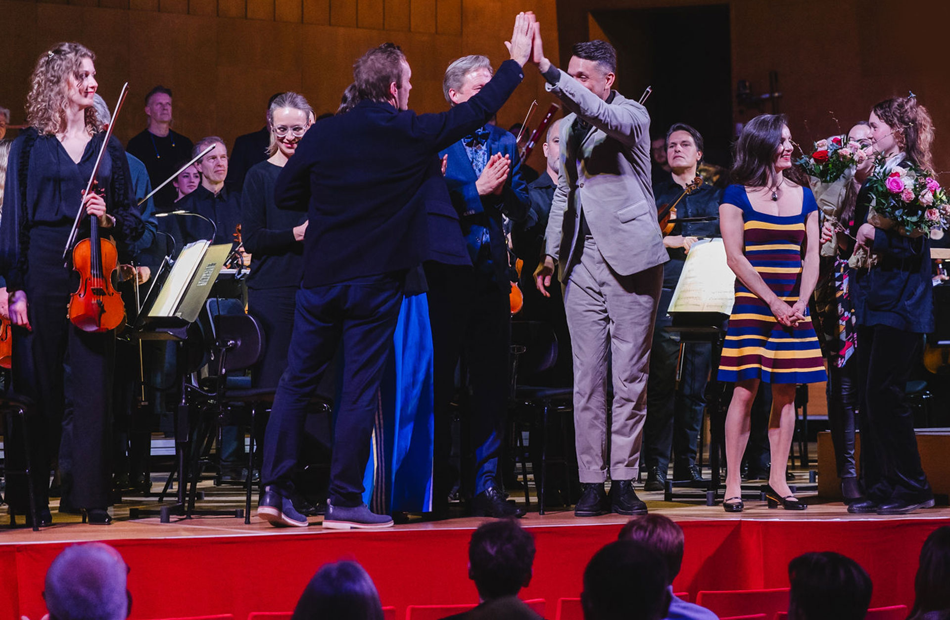 Glada personer på scenen efter konsertens slut, blommor är på väg att delas ut.