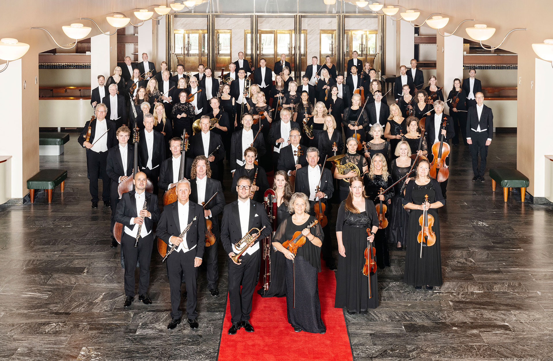 Orkesterns musiker med instrumenten i handen på röda mattan.