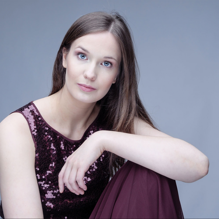 Porträtt av en ung med långt hår som sitter med armen stödd på ett uppdraget knä. Hon tittar in i kameran.