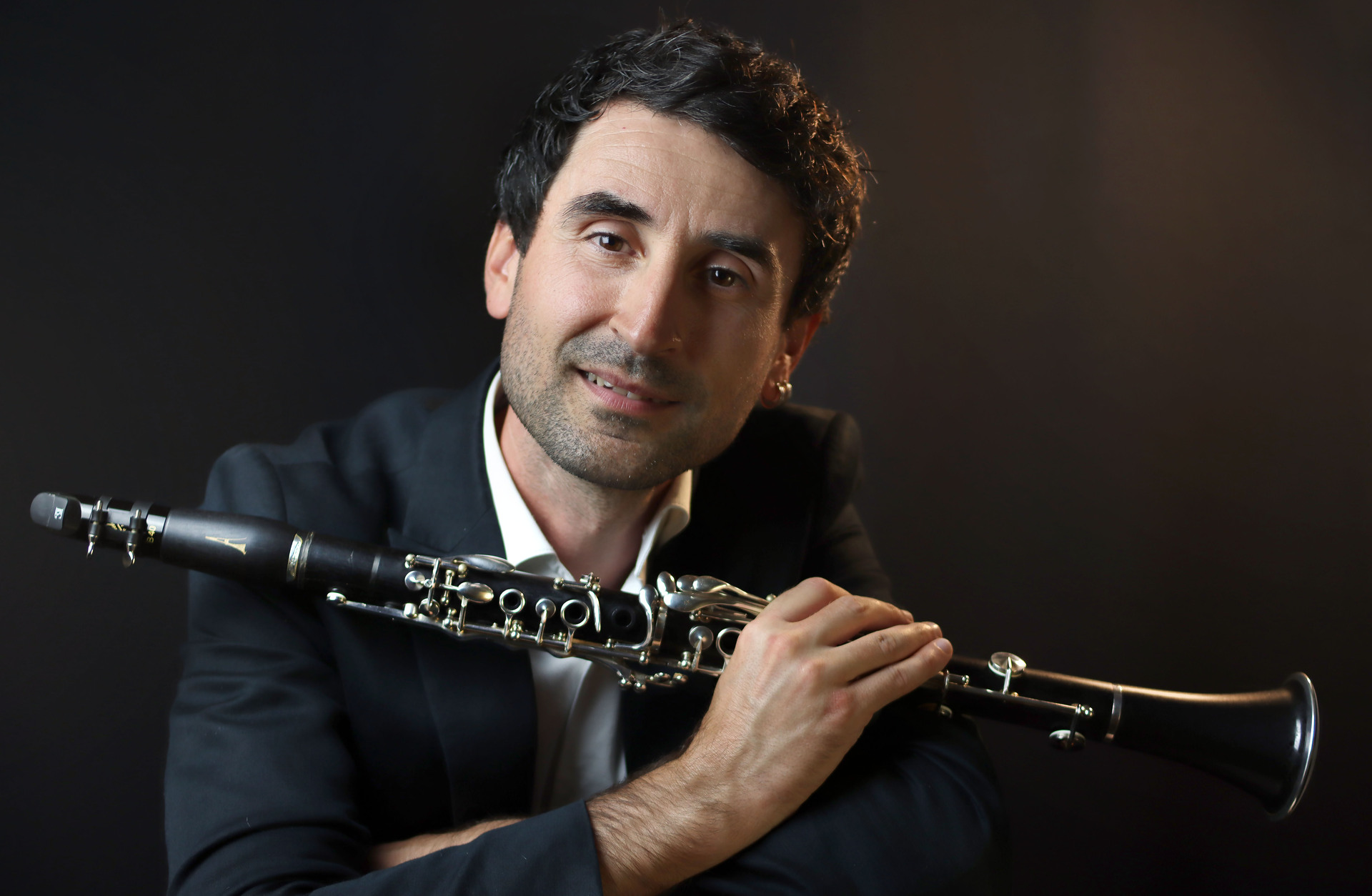 En makedonsk-svensk klarinettist sitt med en klarinett i handen, han har en mörk kostym på sig.