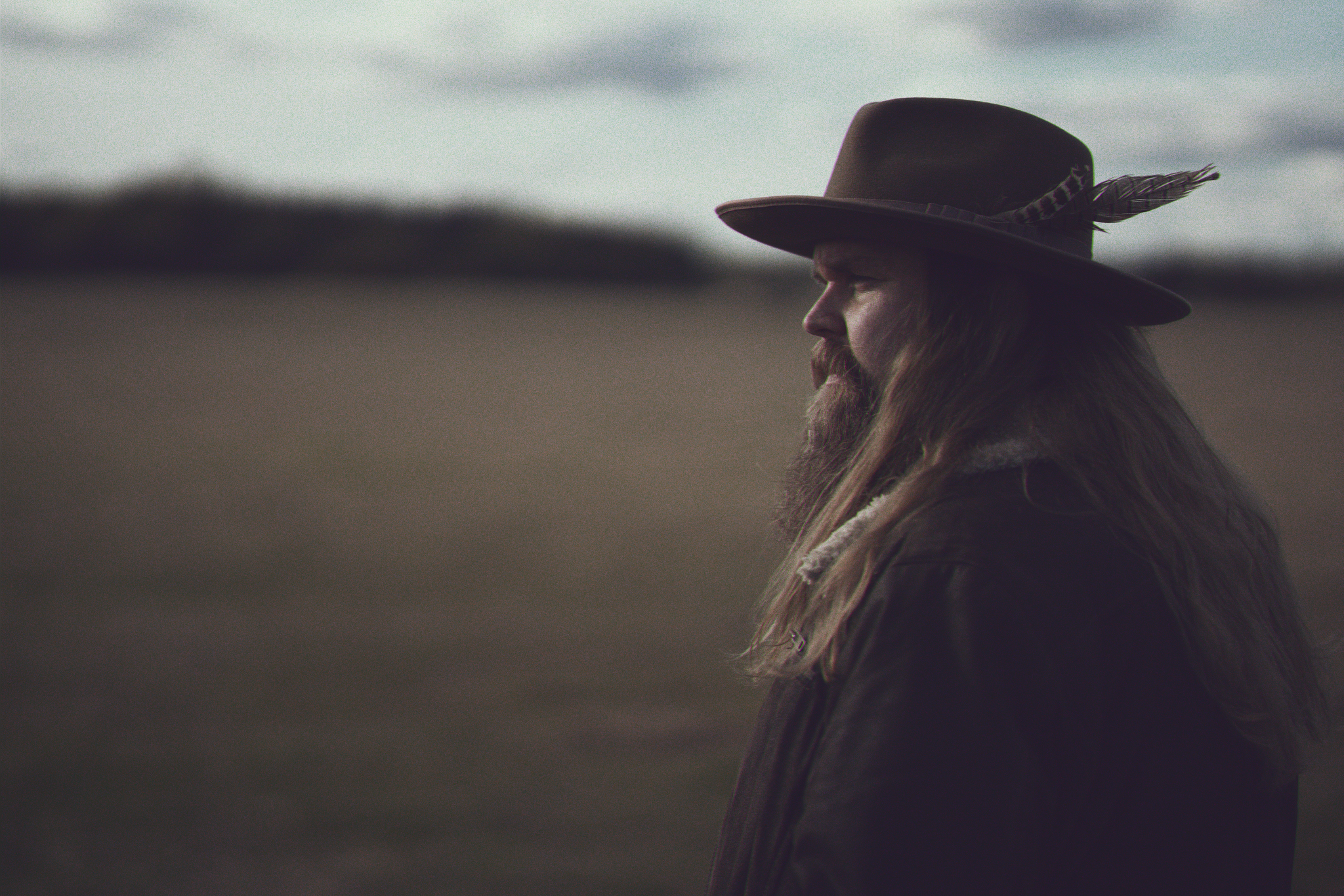 En man med hatt står i öknen, han har långt hår och skägg