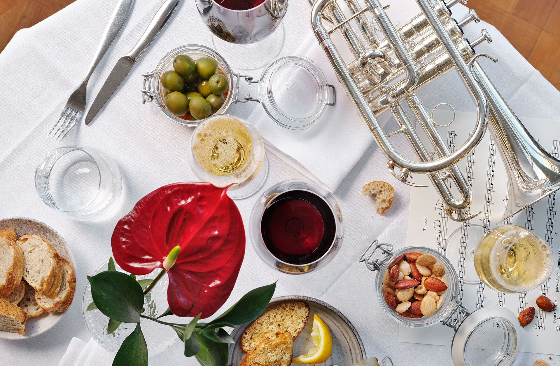 Bord med vit duk, röd blomma, hrälig plockmat som oliver, brlöd och mandlar, samt en kornett i silver.