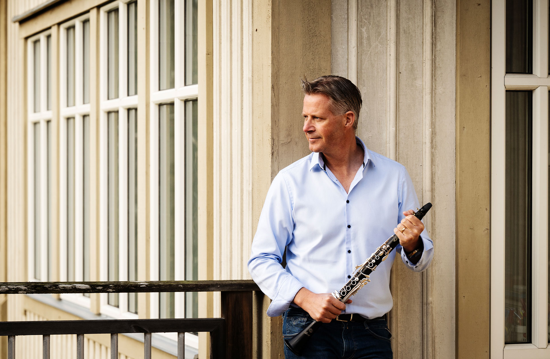 Henrik Nordqvist, en medelålders man klädd i jeans och skjorta står utomhus med en klarinett i händerna.