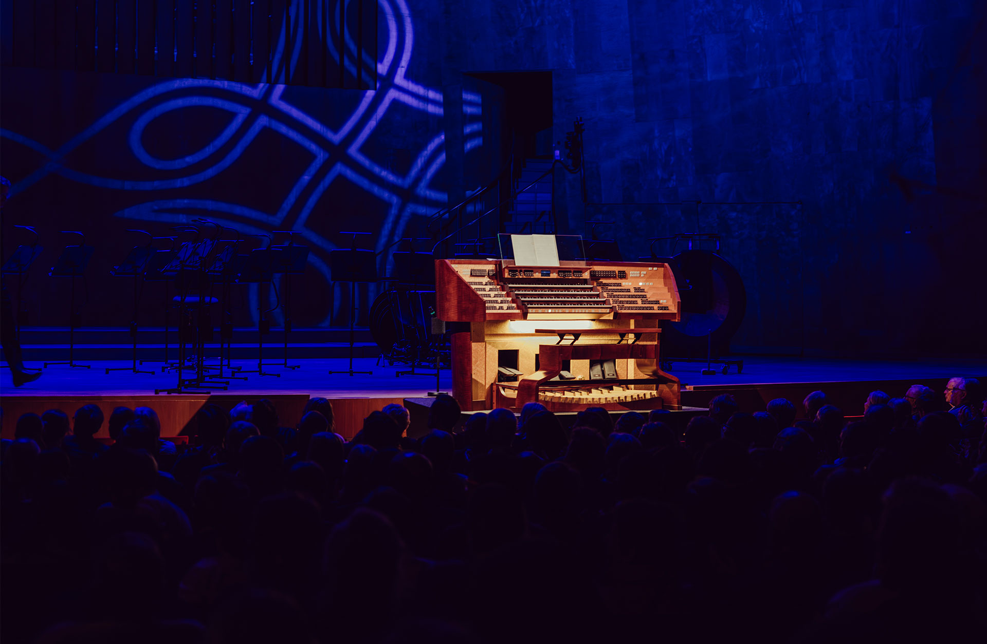 Orgelns spelbord står i strålkastarljus på podiet. Man ser publikhuvuden i förgrunden.