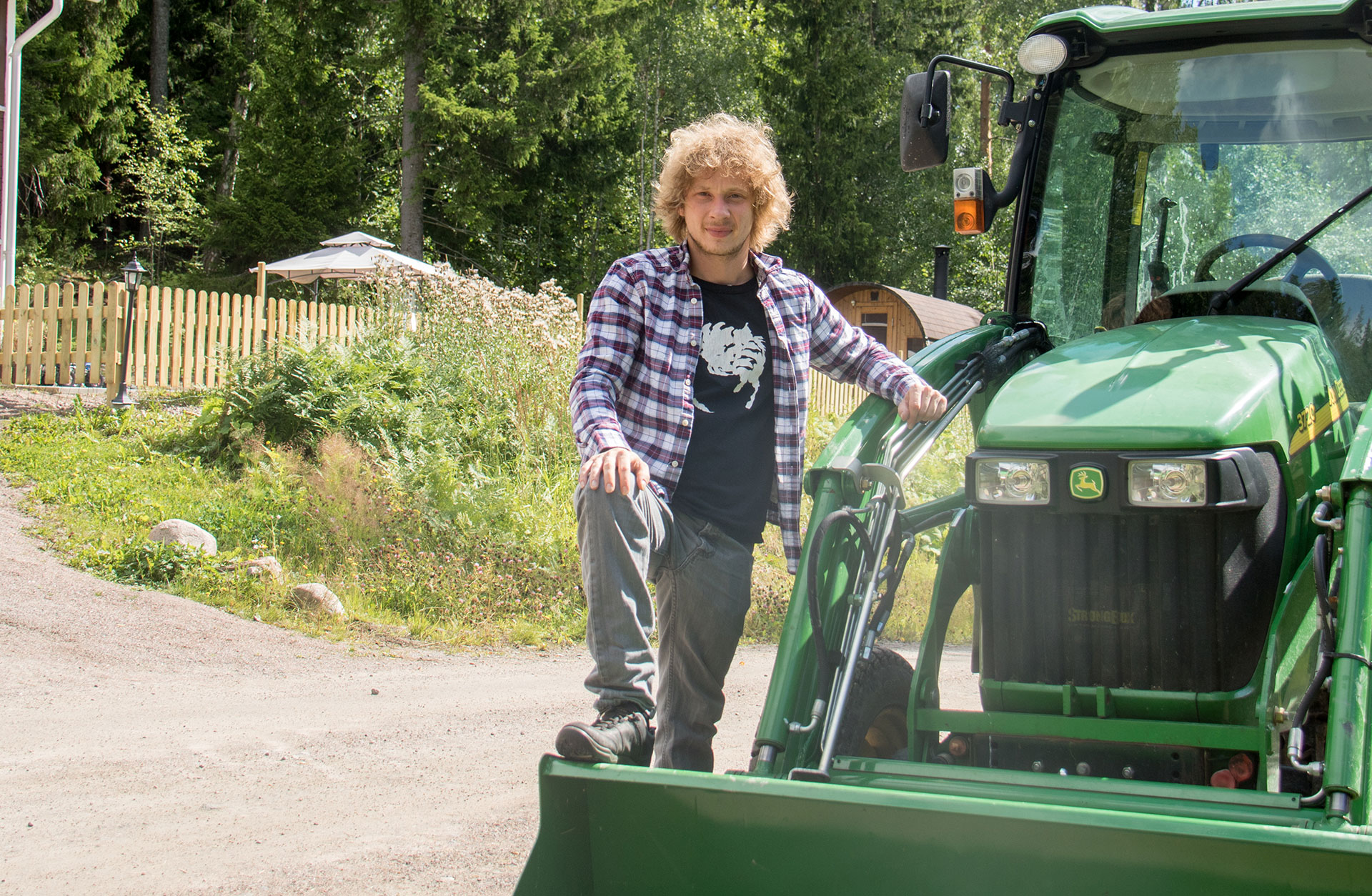 Santtu-Matias Rouvali står vid en grön traktor. Han är klädd i jeans och rutig flanellskjorta.