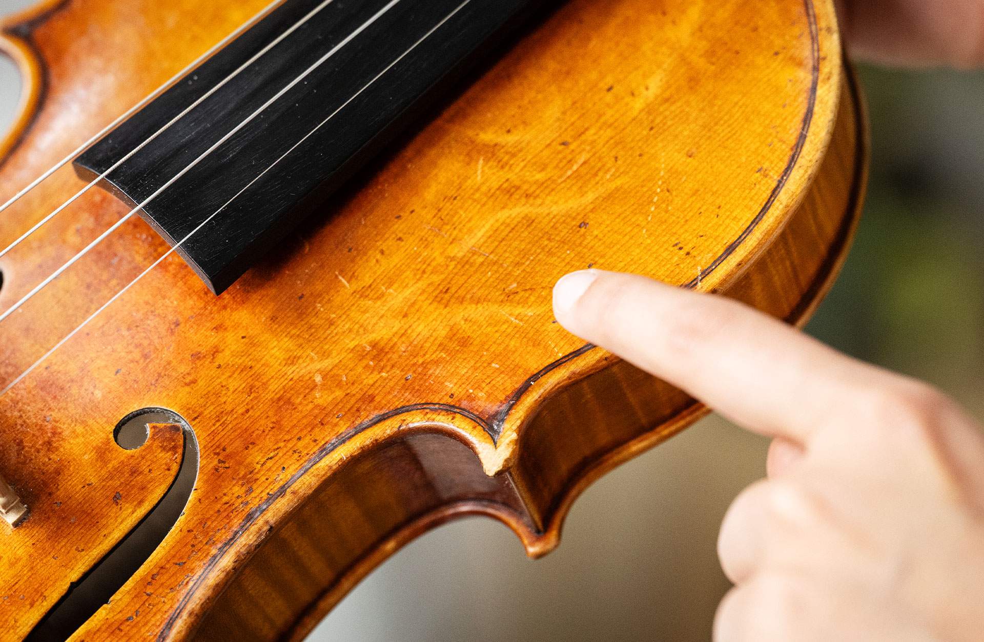 Trädetaljer av en fiol. Ett finger pekar på ytan.