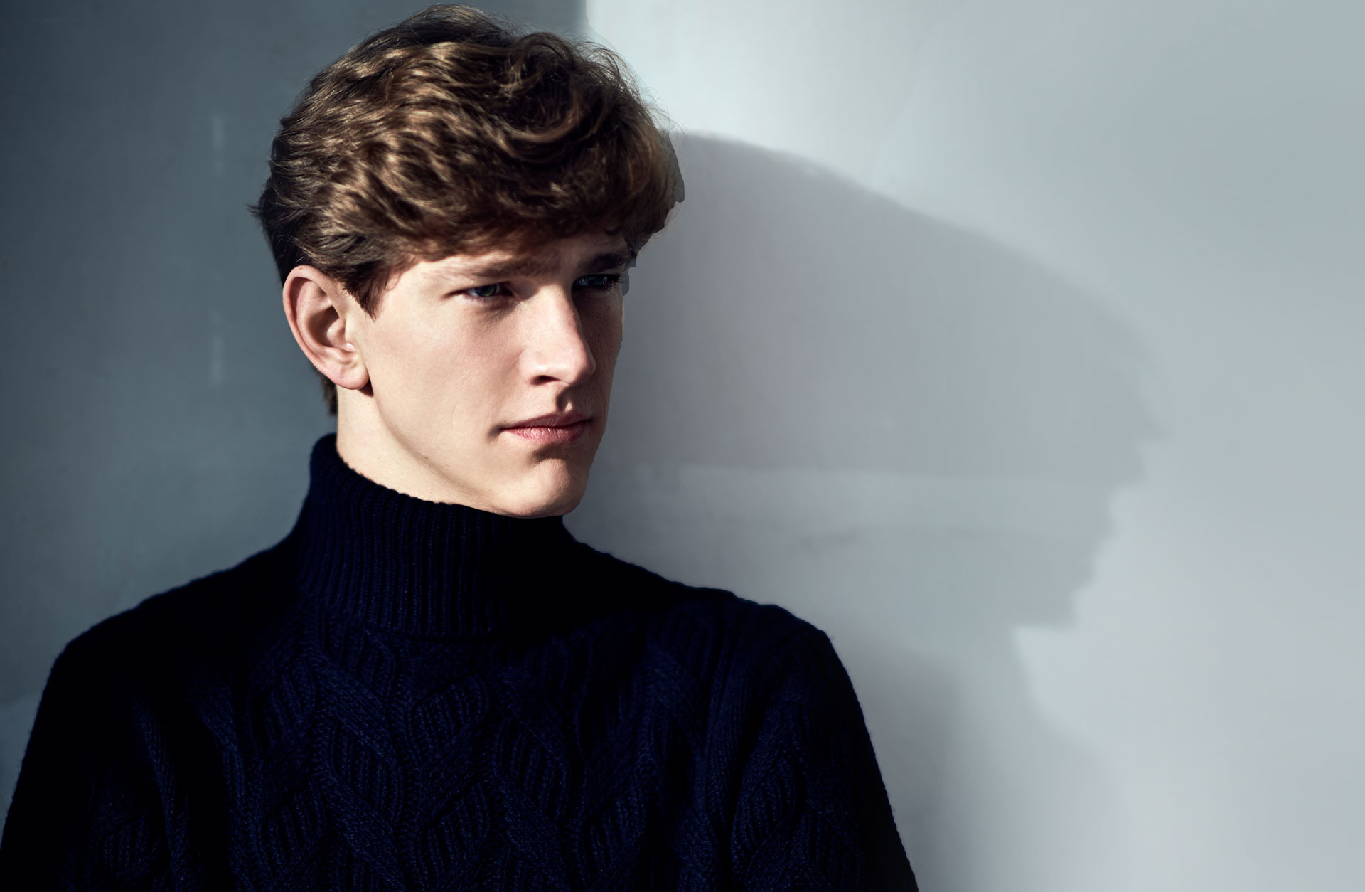 Porträtt av en en ung man med svart polotröja. Han står halvt i profil och tittar bort.