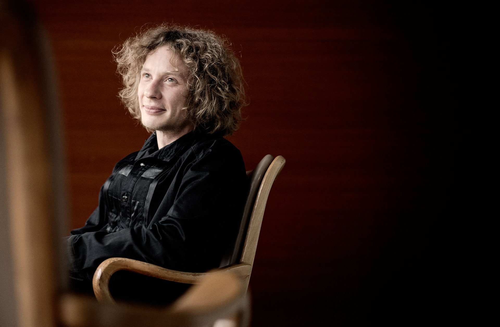 Santtu-Matias Rouvali siter i en stor. Man ser honom från sidan. Han tittar förbi kameran och ler.