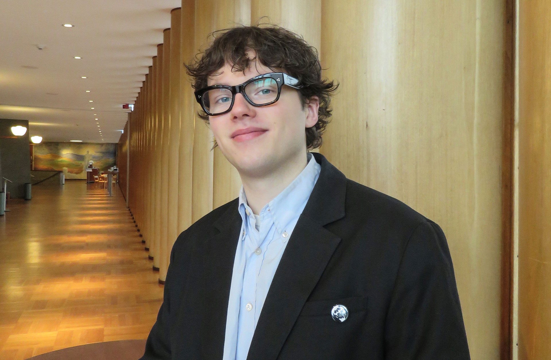 En ung man med kort hår och glasögon står i Konserthusets foajé. Han ler mot kameran.