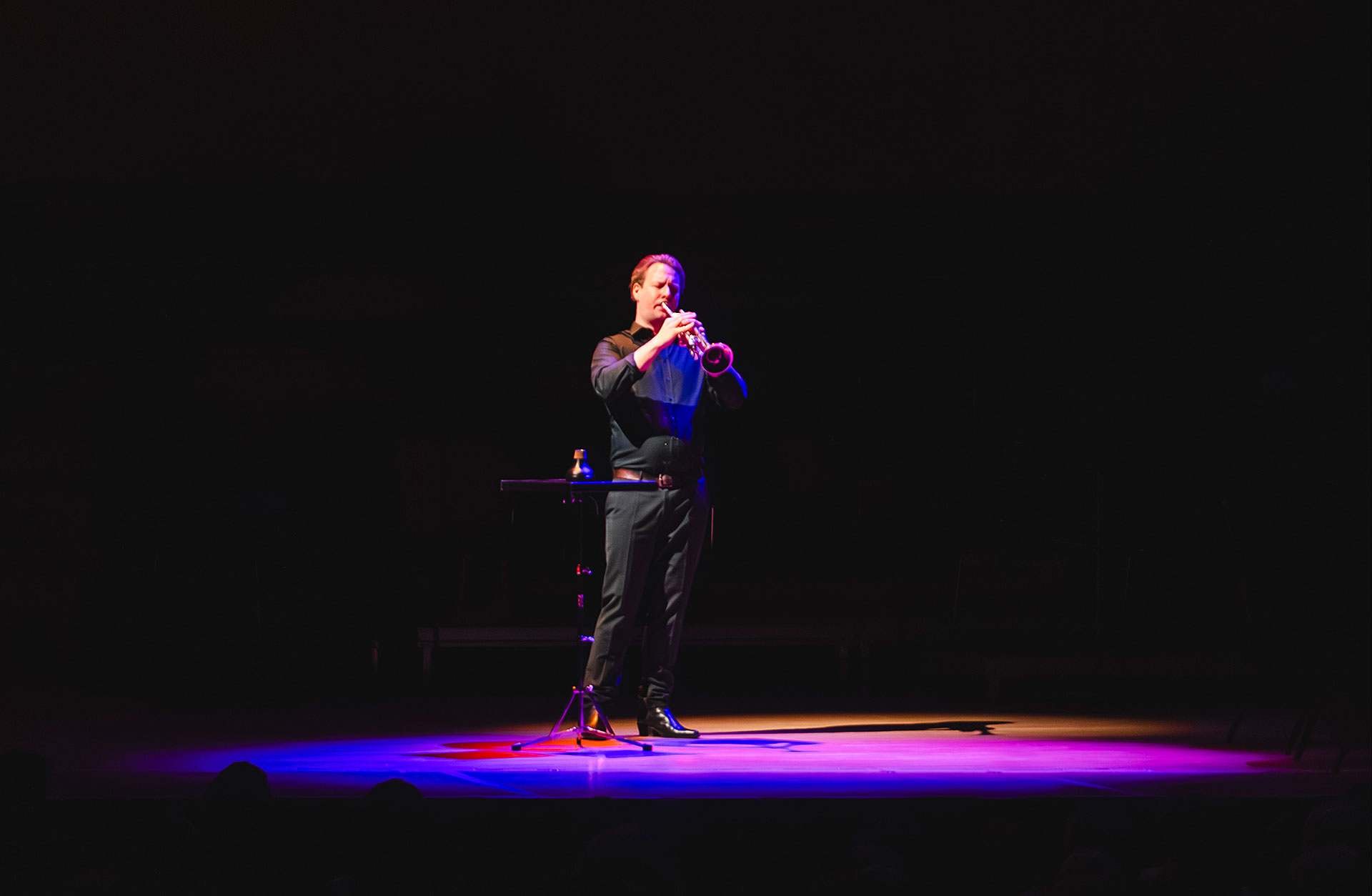 Man spelar trumpet i svart rum med lila ljus på sig.