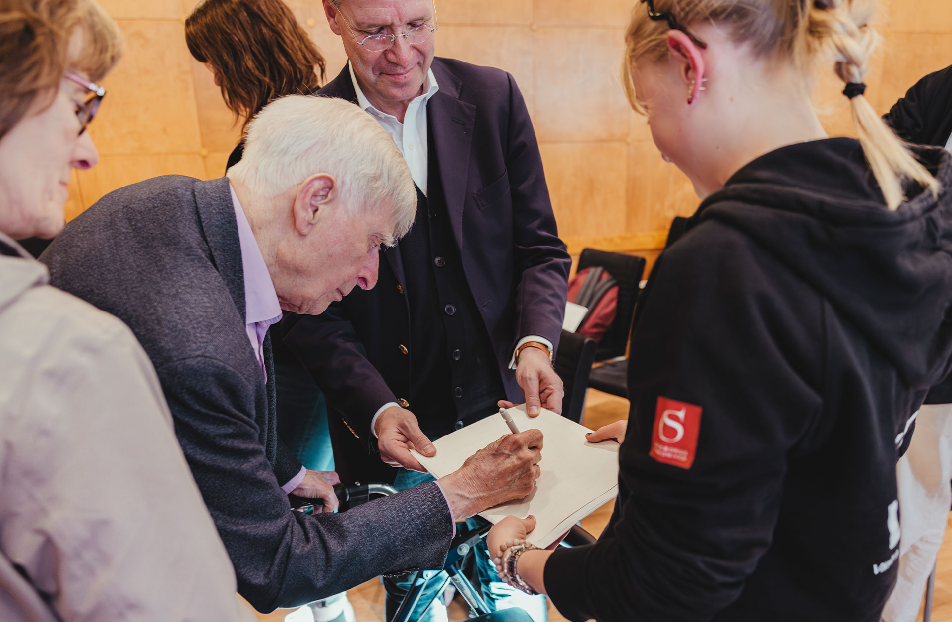 En äldre man skriver sin autograf på ett block.