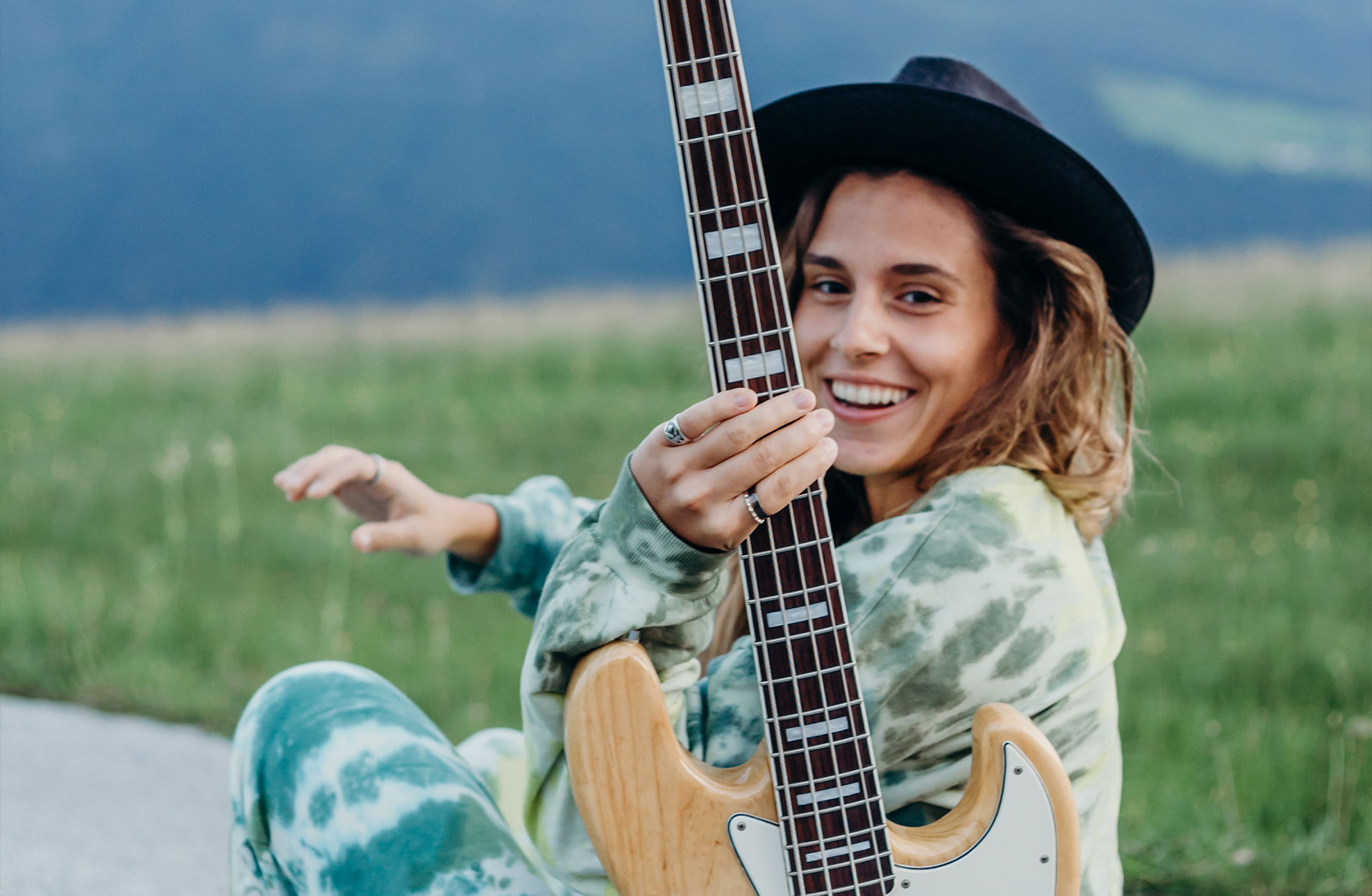 En glad kvinna i hatt håller i en elbas.