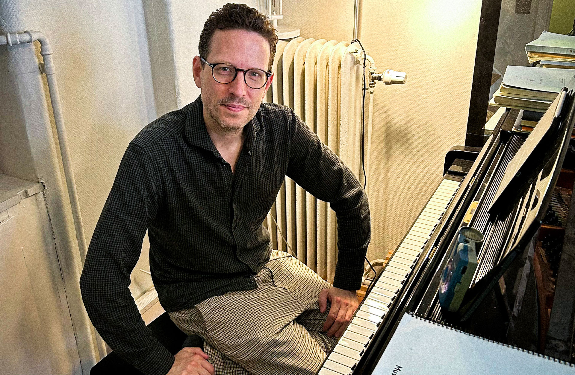 En man sitter vid en flygel och ler mot kameran.