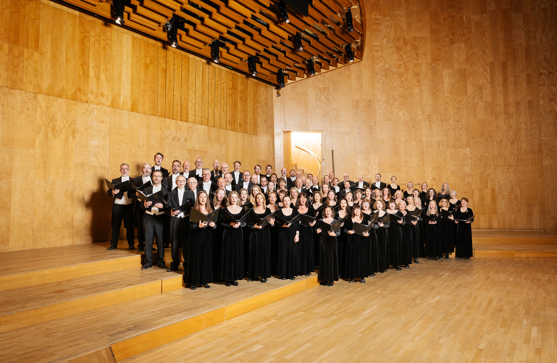 Bild på en finklädd grupp med kvinnor och män som står på Konserthusets stora scengolv. De bär konsertkläder.