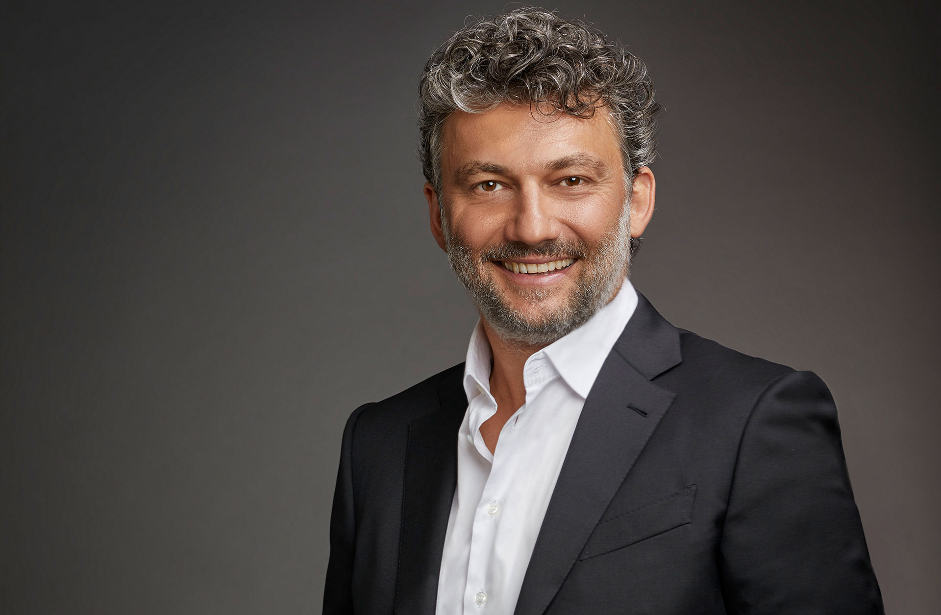 En glad man i vit skjorta och kavaj, ler mot kameran.