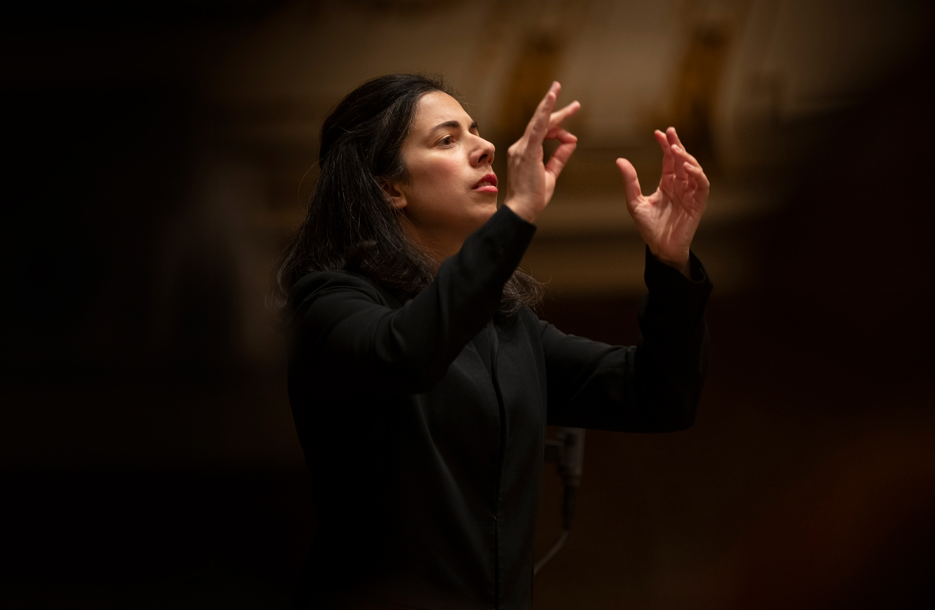 En kvinna med långt hår dirigerar en orkester med händerna.