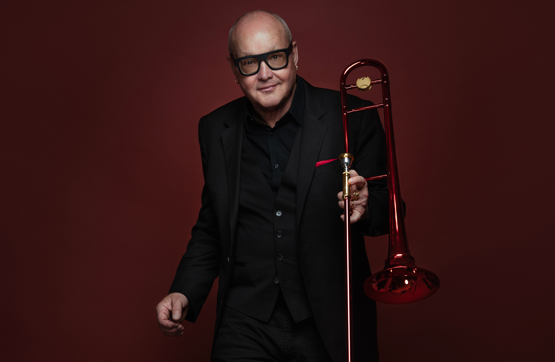 Nils Landgren, i svart kostym och svarta glasögonbågar, håller i en trombon.