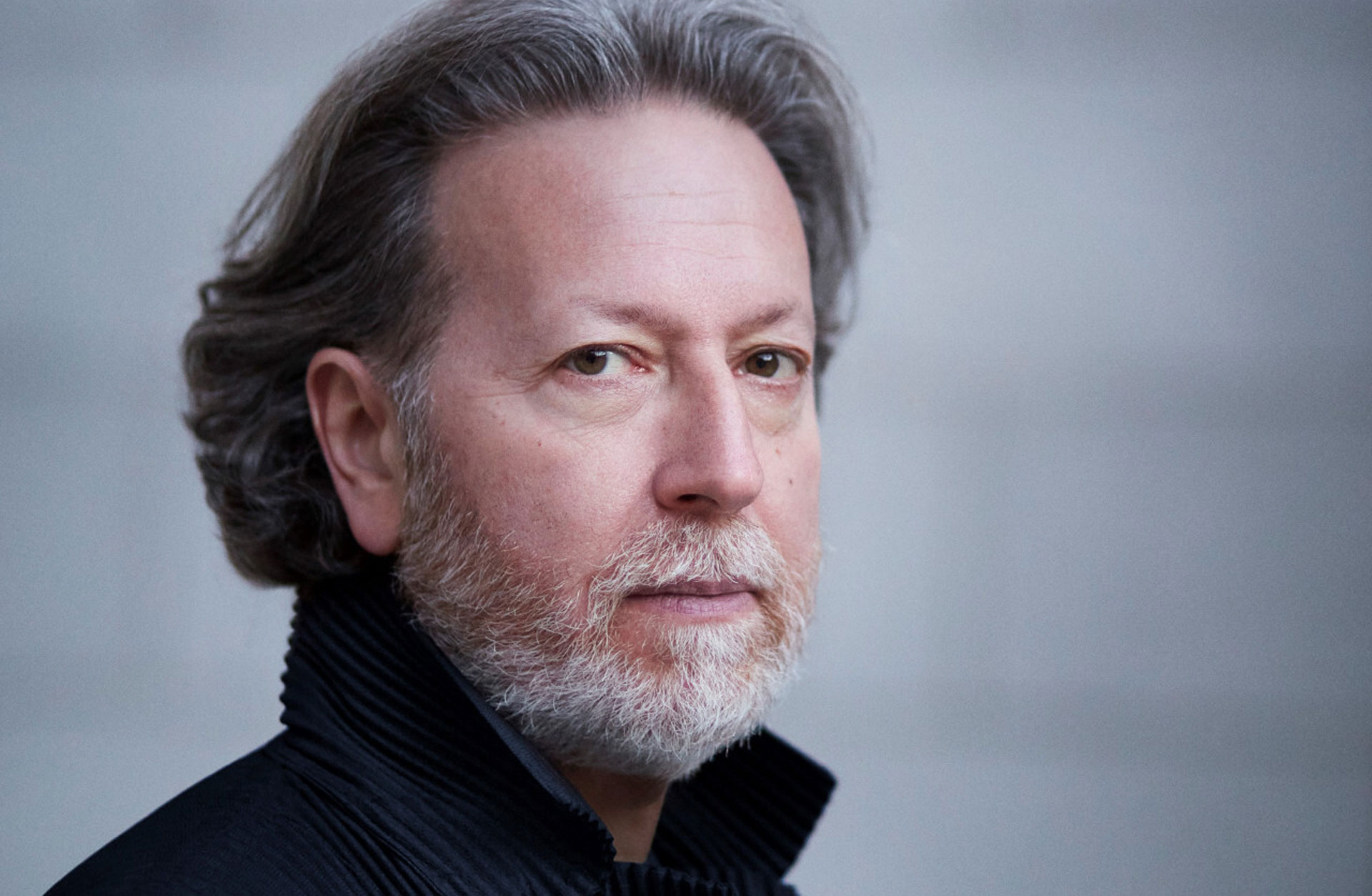 Dirigent Brad Lubman. Porträttbild tagen från sidan. Dova färger. Han tittar in i kameran.