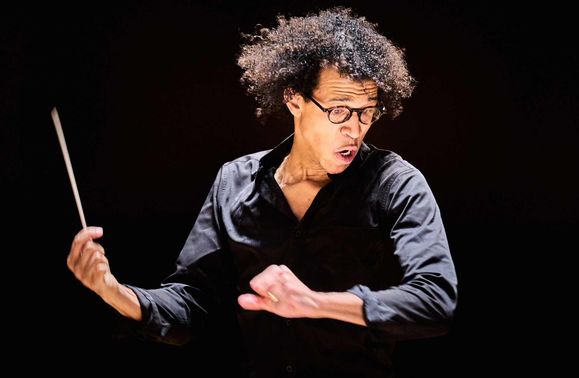 Dirigent in action mot mörk bakgrund. Intensiv bild där håret flyger i luften.