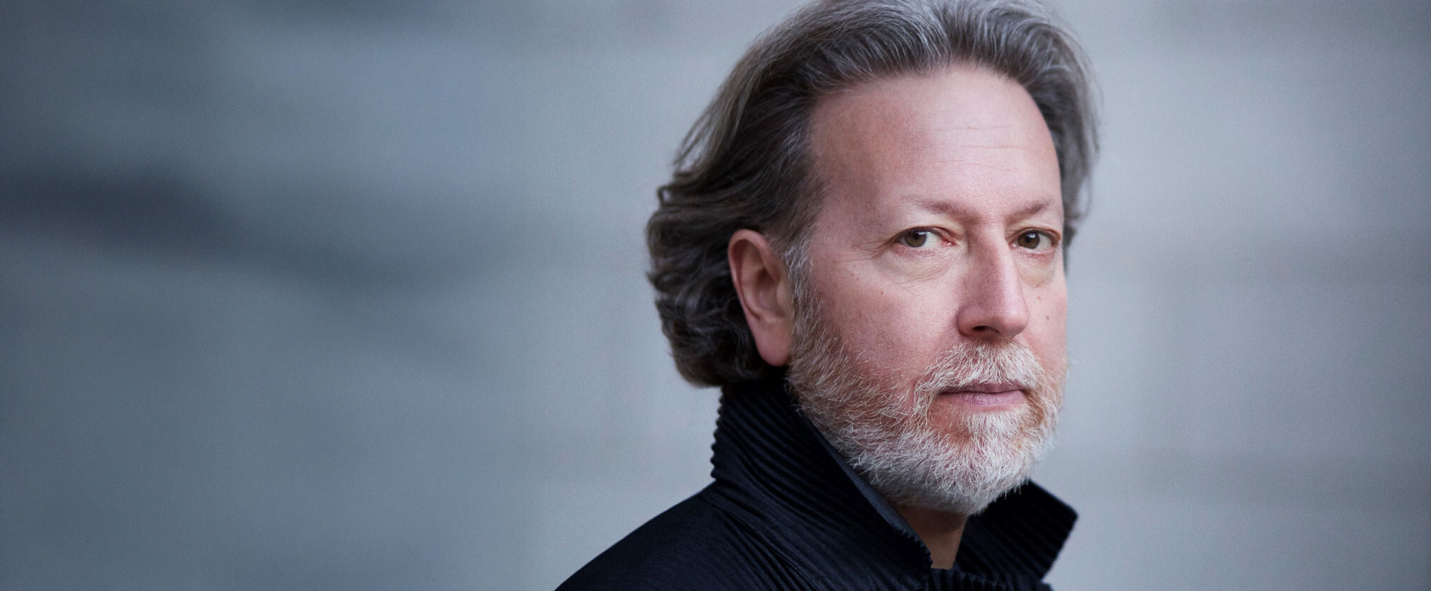 Dirigent Brad Lubman. Porträttbild tagen från sidan. Dova färger. Han tittar in i kameran.