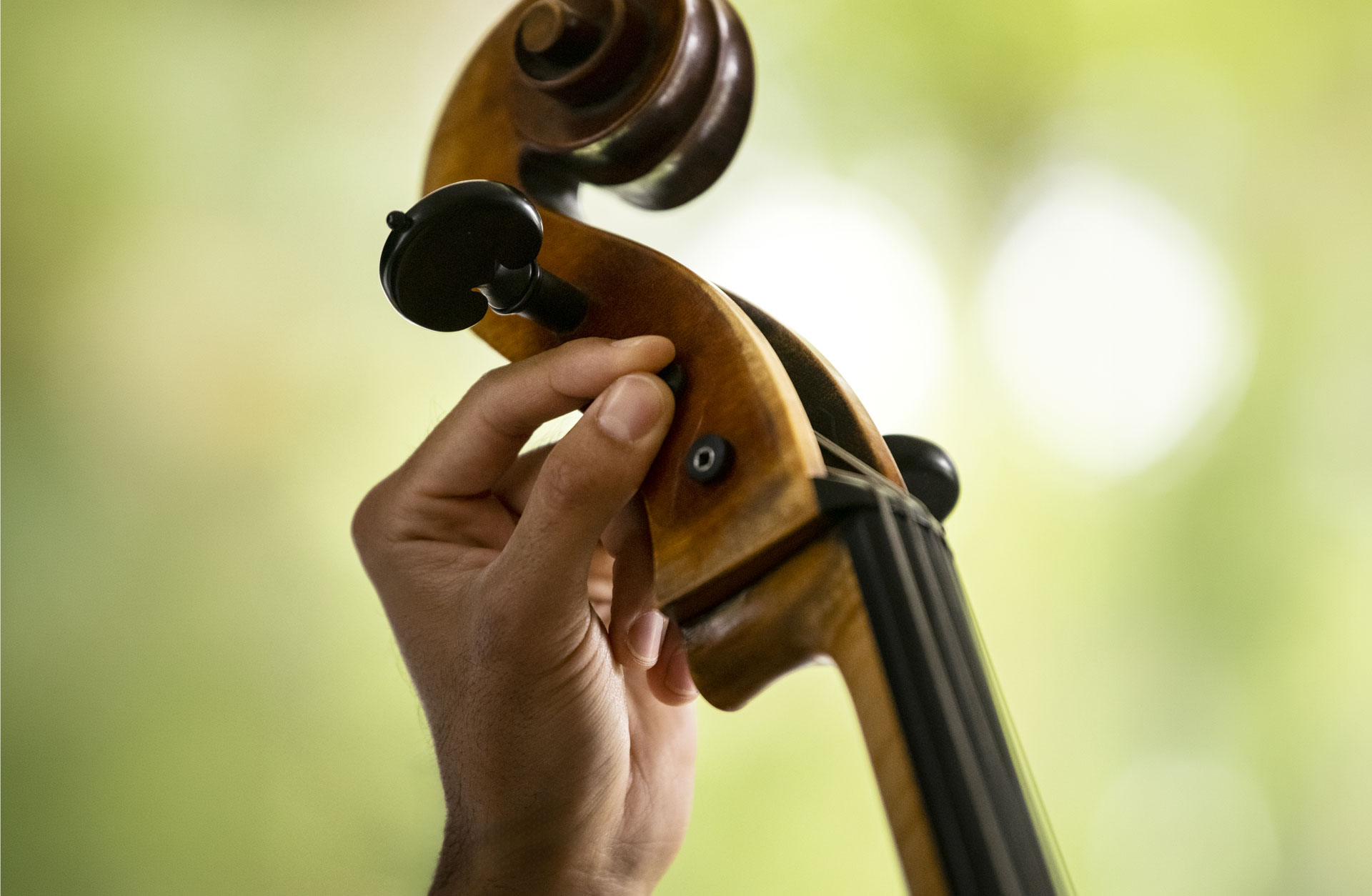 En hand stämmer en cello, närbild på fingrarna på stämskruven.