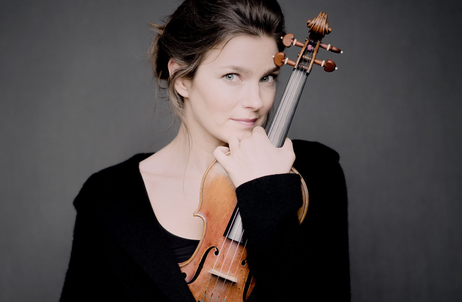 En kvinna i uppsatt mörkt hår och svart tröja håller om sin fiol.
