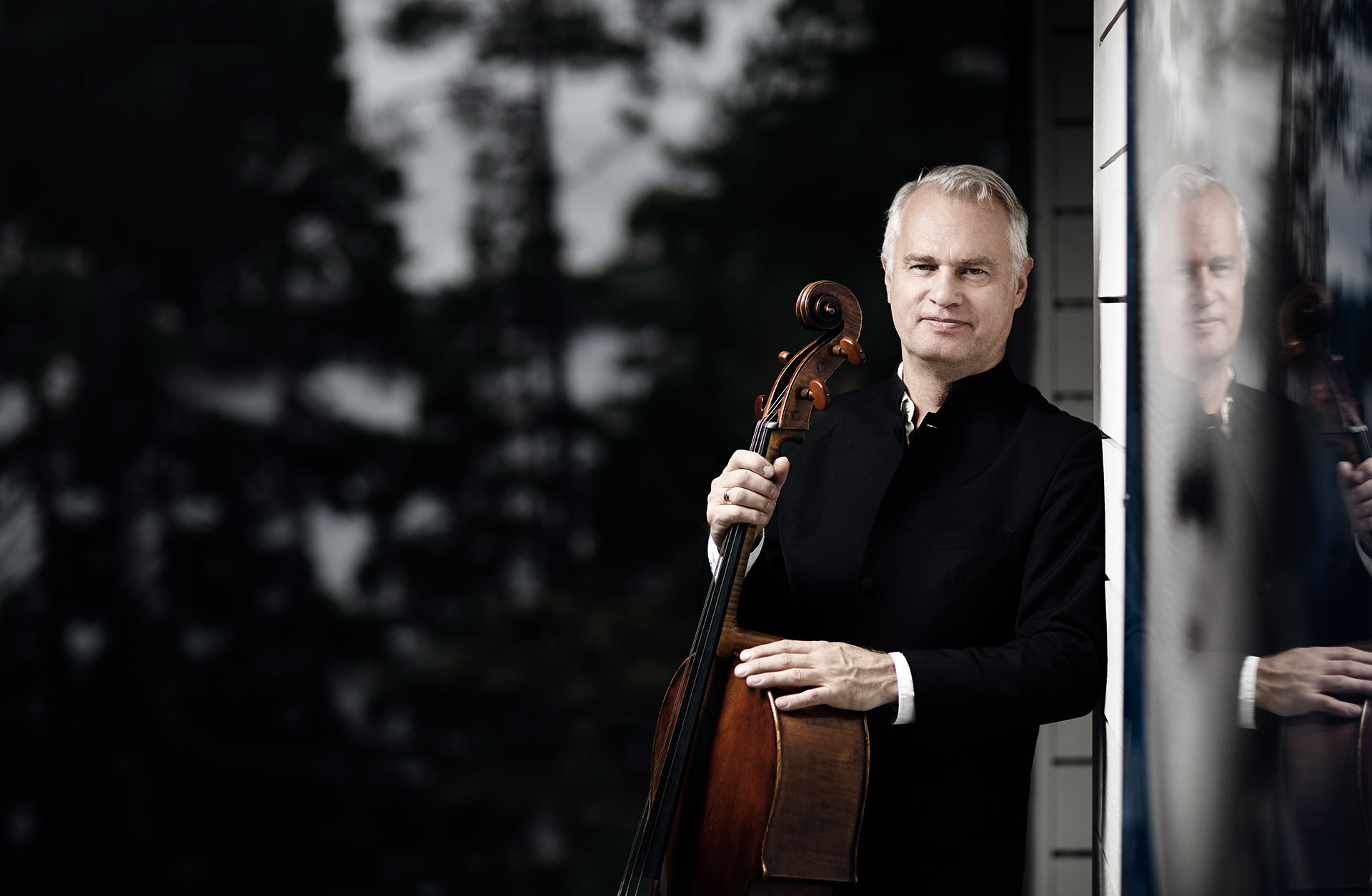 Leende man lutar sig mot en vägg med en cello i handen.