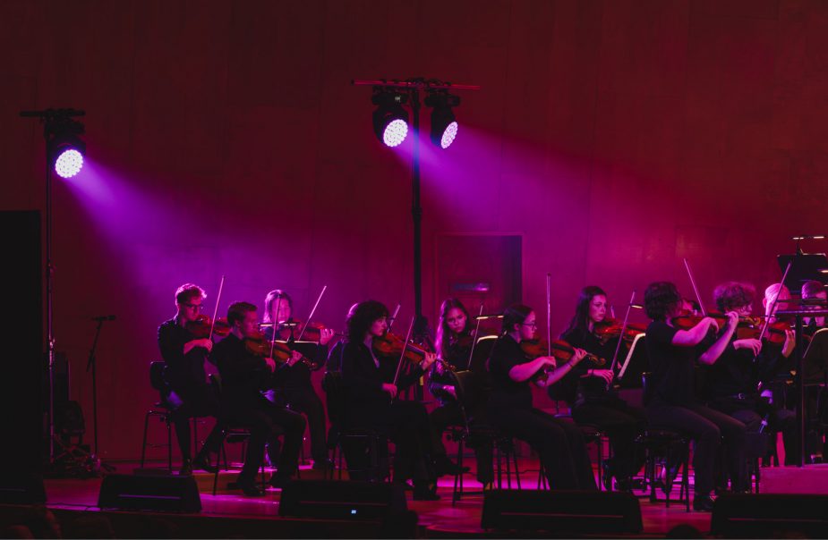 En orkester sitter på podiet i strålkastarljus.