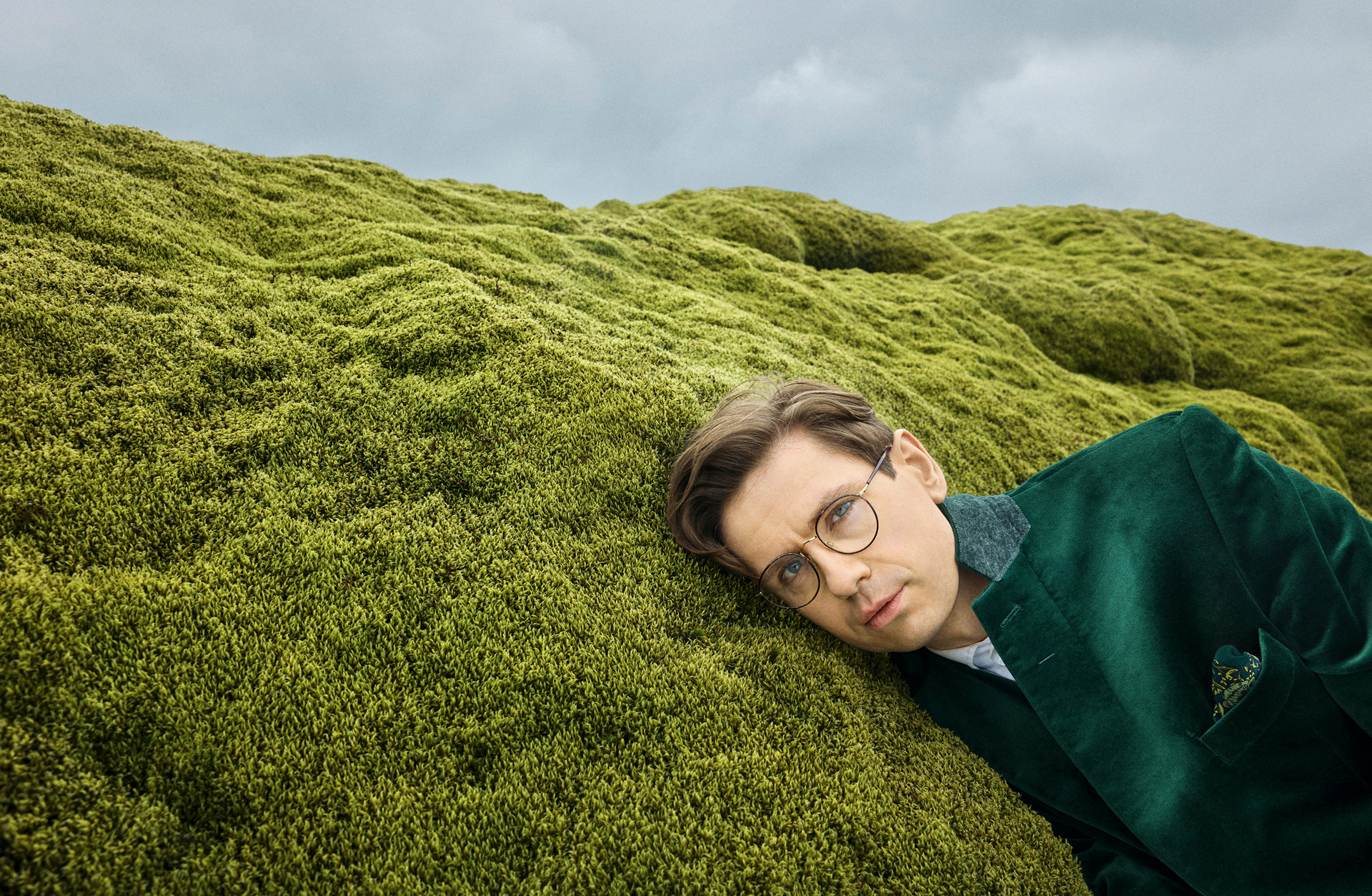 En man i grön kostym ligger på en gräsbetäckt kulle.