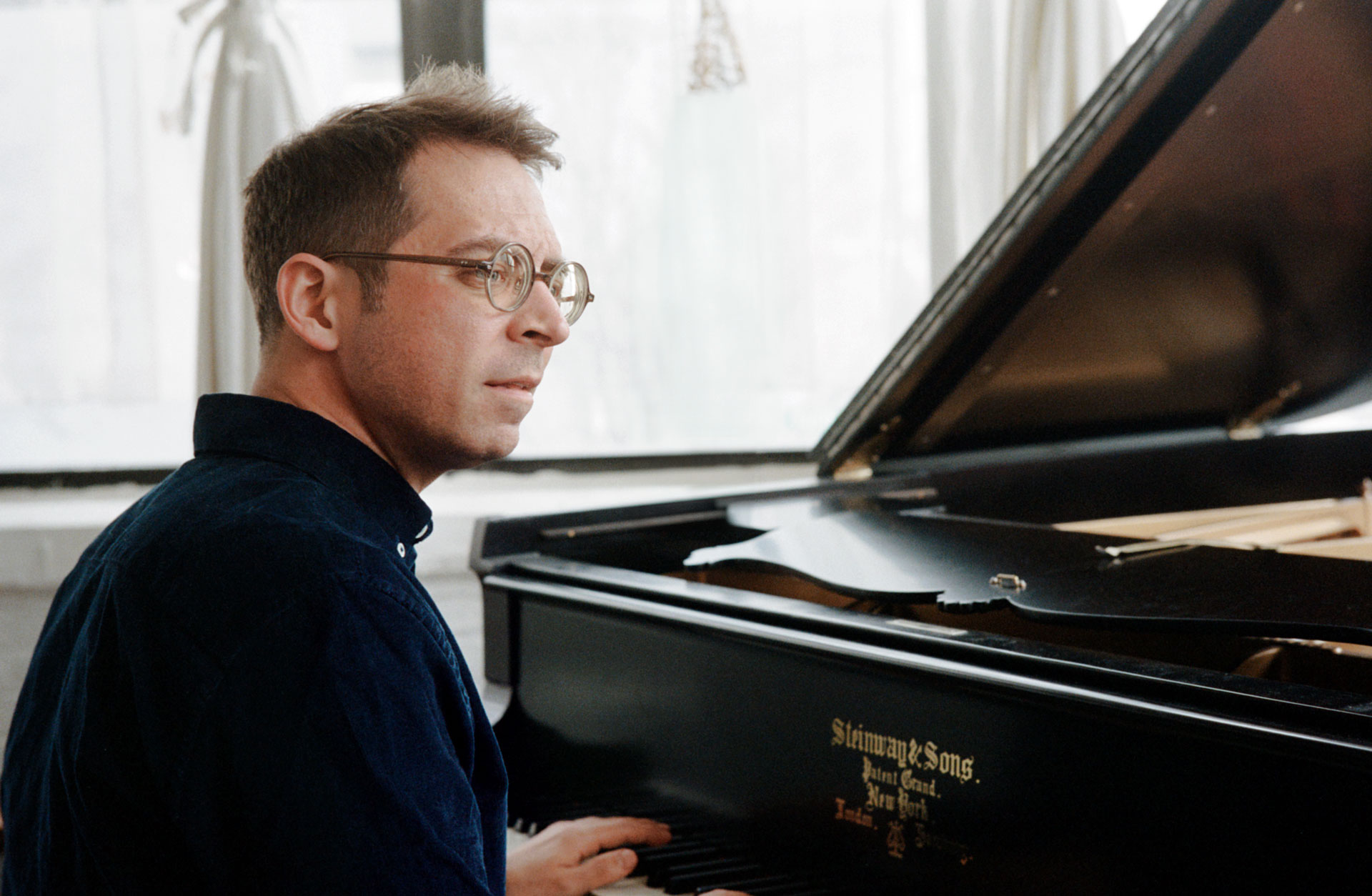 Pianist sitter med ryggen åt kameran och tittar åt sidan. Framför honom syns pianot.