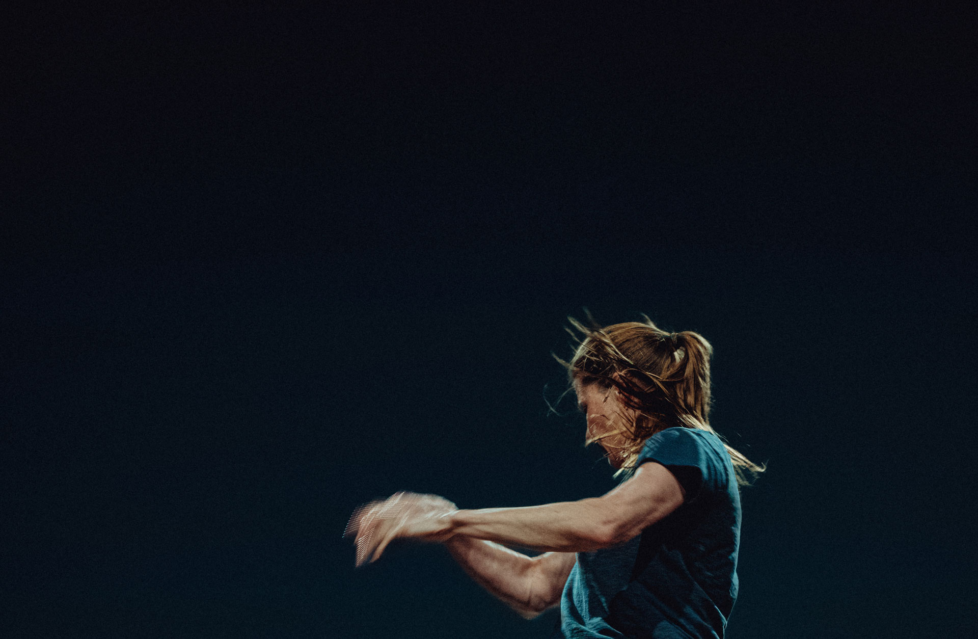 Barbara Hannigan. Bild tagen från sidan medan hon dirigerar. Mörk bakgrund.