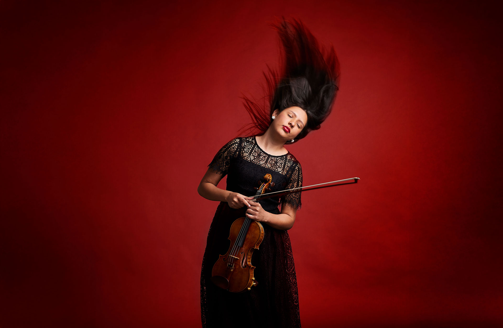 Violinist slänger med huvudet så det långa håret flyger i luften. Röd dramatisk bakgrund.