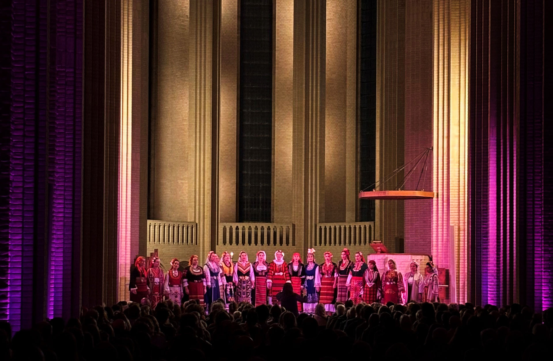 Kör på pampig scen. Rosa ljus lyser upp de många körmedlemmarna.