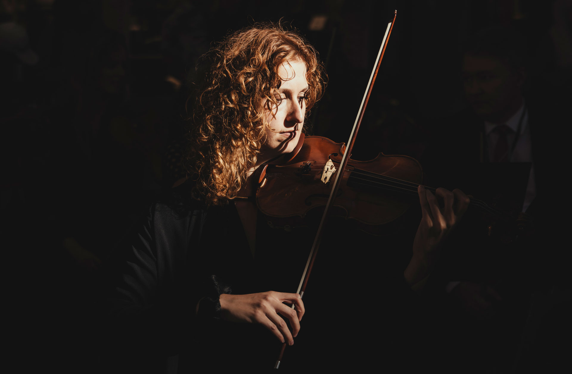 Violinist Clara Garde står i mörk omgivning och spelar violin