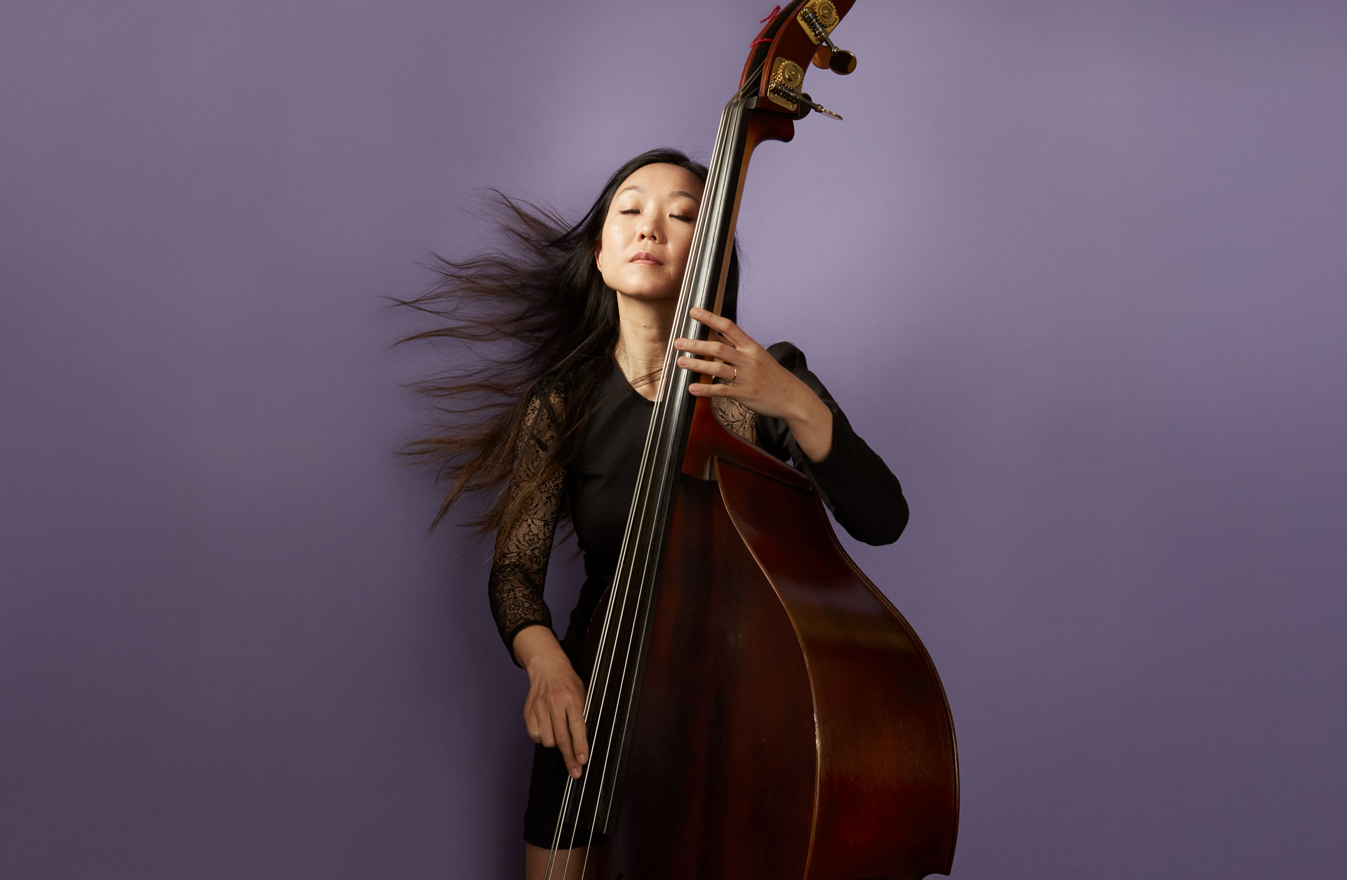 En kvinna spelar på en kontrabas. Hennes långa svart hår flyger åt vänster.