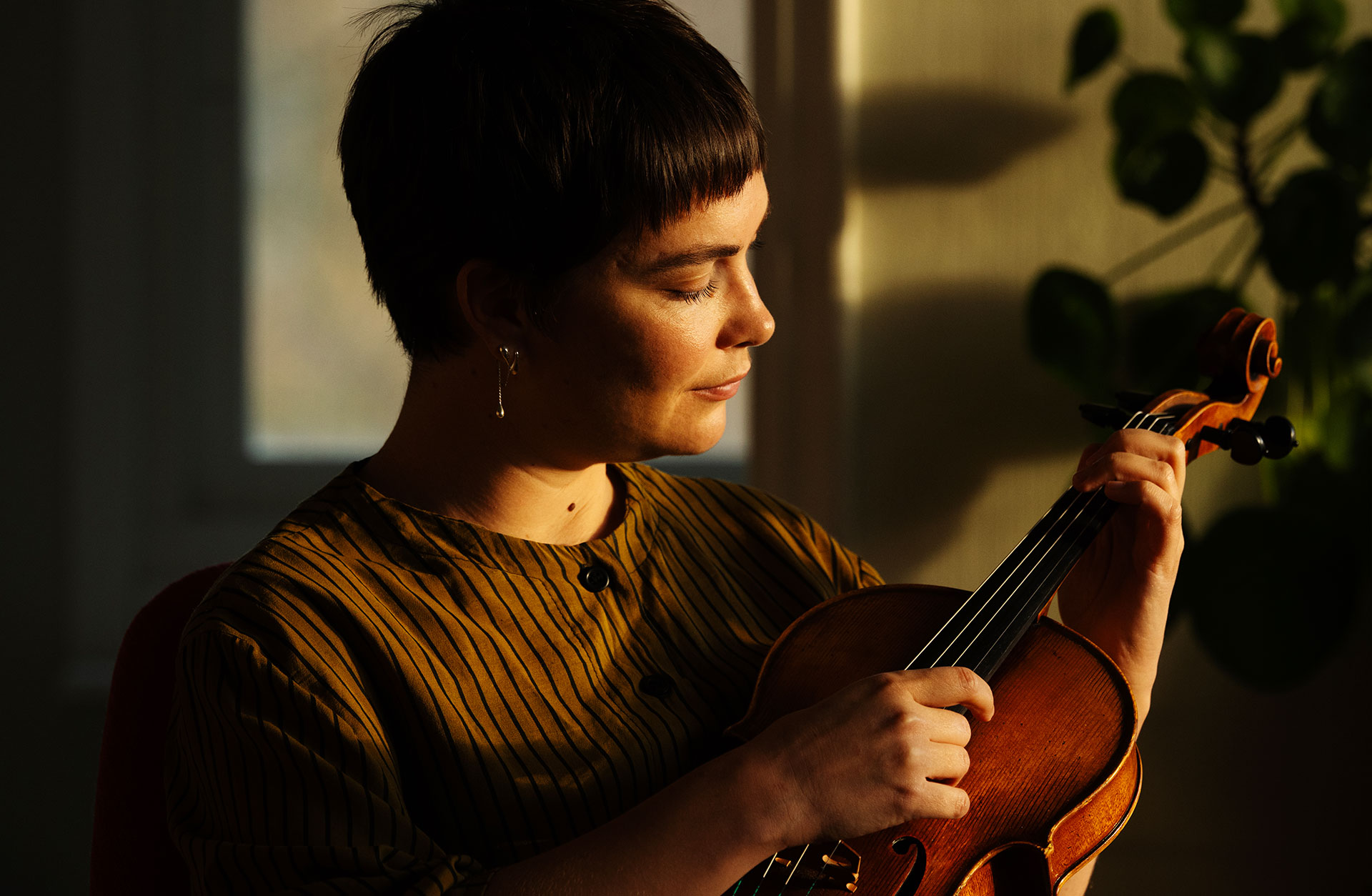 En kortklippt kvinna sitter med sin fiol och klinkar på strängarna.